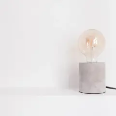 Bombilla Edison de cristal transparente sobre base de cemento gris con cable negro.