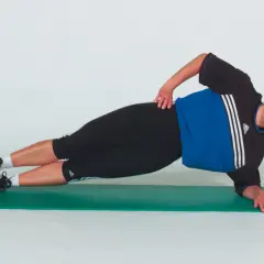 Donna in posizione di lato su un tappetino verde, esegue un esercizio di plank laterale per rafforzare il core.