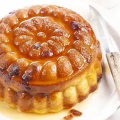 Gâteau de semoule doré et moelleux, nappé d'un sirop ambré et parsemé de raisins secs. Un couteau est posé à côté, prêt à découper cette gourmandise.