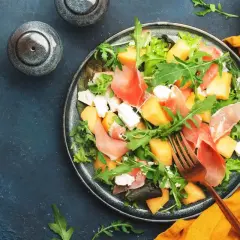 Insalata con melone, prosciutto crudo e formaggio fresco, guarnita con rucola. Un piatto estivo perfetto.