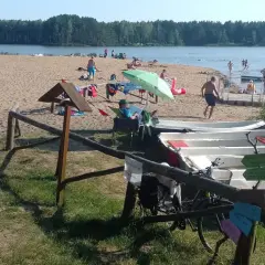 Słoneczny dzień nad zalewem zielona. Ludzie odpoczywają na plaży, kąpią się w wodzie, a obok cumują łódki.