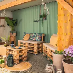 Gemütliche Sitzecke im Hof gestalten mit Palettenmöbeln, bunten Kissen und Lichterkette. Einladend und stilvoll.
