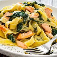 Pappardelle z łososiem i szpinakiem, danie fit, podane na białym talerzu z widelcem i nożem.