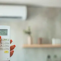 Mano con control remoto para cambiar temperatura aire acondicionado. Pantalla muestra 25°C.
