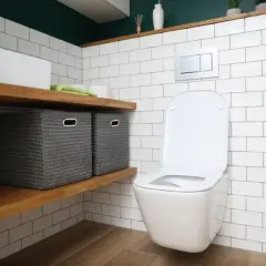 Nowa deska wolnoopadająca do toalety. W łazience białe kafelki, drewniane półki z koszami i nowoczesna miska WC.
