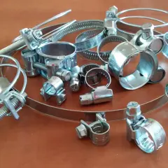Metalowe opaski zaciskowe, czyli trytytki, w różnych rozmiarach, leżą na drewnianym blacie.