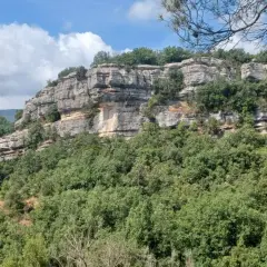 Falaises calcaires spectaculaires des gorges du Caramy, couvertes de végétation luxuriante sous un ciel bleu et nuageux.