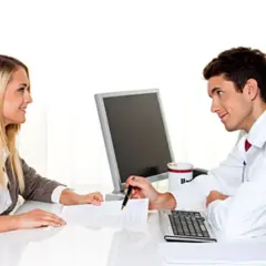 Arzt erklärt einer Frau, was passiert, wenn man die private Krankenversicherung nicht bezahlt. Sie besprechen Dokumente am Schreibtisch.