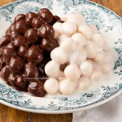 Pignolata messinese: palline dolci ricoperte di cioccolato fondente e glassa bianca, servite su un piatto decorato.