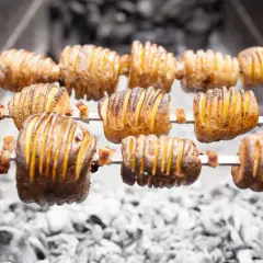 Pommes de terre coupées en accordéon, grillées à la broche sur des braises. Quelle pomme de terre barbecue !