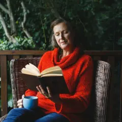 Kobieta w czerwonym swetrze czyta ambitne książki warte przeczytania, popijając kawę na werandzie.