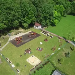 Plac zabaw w otoczeniu zieleni, z huśtawkami, zjeżdżalniami i piaskownicą. W tle budynek i las. To idealne miejsce na wypoczynek dla rodzin z dziećmi w okolicy księża góra radzionków.