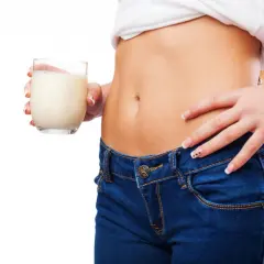 Donna con jeans e maglietta bianca tiene un bicchiere di latte. Un aiuto per capire cosa bere per andare in bagno velocemente.