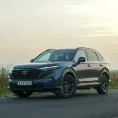 Ciemnoniebieski Honda CR-V Hybrid na tle zachodzącego słońca, zaparkowany na poboczu drogi.