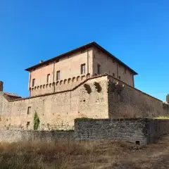 Rocche e mura antiche a Civitella Paganico cosa vedere: un castello medievale in mattoni rossi sotto un cielo azzurro, circondato da vegetazione rigogliosa.