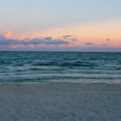 Plaża nad Bałtykiem o zachodzie słońca z różowymi chmurami i spokojnym morzem.