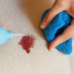 Ręce czyszczą plamę z krwi na kanapie niebieską ściereczką i aplikatorem.