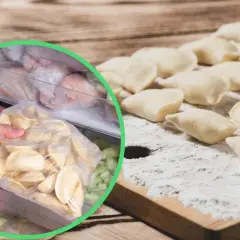 Ręka wkłada do zamrażarki worek z surowymi pierogami, obok leżą uformowane pierogi na desce.