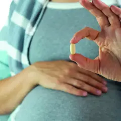 Mujer embarazada muestra una pastilla, una solución para saber como quitar acidez estomago.