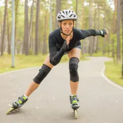 Kobieta w kasku i ochraniaczach jeździ na rolkach po leśnej ścieżce. Czy jazda na rolkach odchudza? Tak, to świetny trening!
