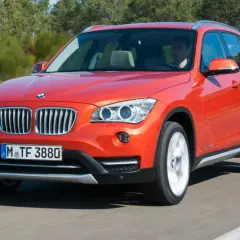 Pomarańczowy BMW E84 w ruchu, z widocznym kierowcą.