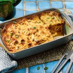Herzhafte Moussaka mit Zucchini, goldbraun gebacken, wartet darauf, serviert zu werden. Ein Stück ist bereits auf einem Teller angerichtet.