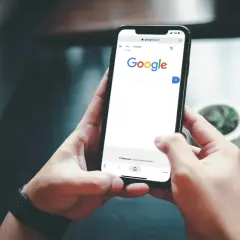 Dłonie trzymające smartfon z otwartą stroną Google.