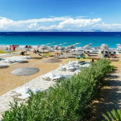 Słoneczna plaża Faliraki by Sun Palace z leżakami i parasolami. Turkusowe morze i góry w tle.