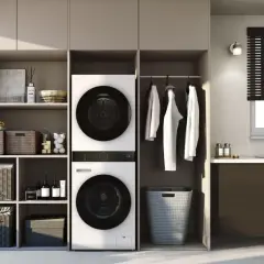 Ein moderner Waschraum mit einem Trockner, der auf einer Waschmaschine steht. Daneben hängen Kleider und ein Wäschekorb.