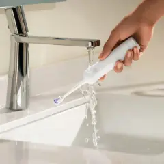 Mano che sciacqua uno spazzolino elettrico sotto un rubinetto. Ideale per chi soffre di gengive ritirate.