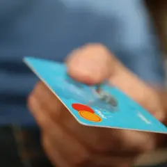 Dłoń trzyma niebieską kartę debetową. Uważaj na podwójnie pobrane pieniądze przy płatności kartą.