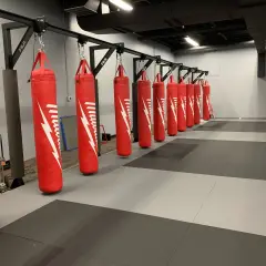A row of red punching bags hangs from a metal rack, demonstrating how to hang a punching bag for optimal training.