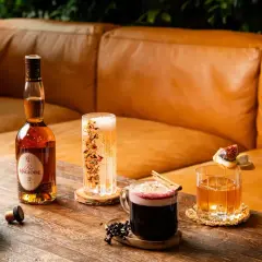 En flaska Calvados står bredvid drinkar och tillbehör på ett träbord.