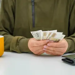 Osoba liczy pieniądze, być może czekając na podwyżki dla pracowników samorządowych. Obok stoi żółty kubek i portfel.