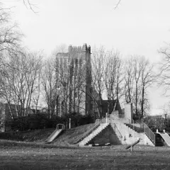 A playground with slides and stairs, captured on Ilford Pan 400 film, stands amidst bare trees with a brick tower in the background.