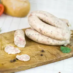 Biała kiełbasa na desce, obok pomidor, chleb i przyprawy. Zastanawiasz się, ile m mają jelita?