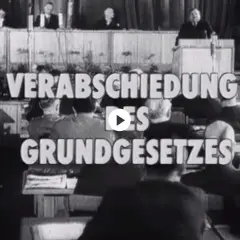 Der parlamentarische Rat verabschiedet das Grundgesetz. Männer in Anzügen sitzen und stehen im Saal.