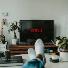 Telewizor z logo Netflix, gitara elektryczna i rośliny w salonie.