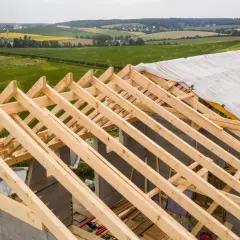 Charpente en bois sur un chantier, recouverte d'une bâche. La question est : combien de temps peut-on laisser une charpente dehors avant qu'elle ne se dégrade ?