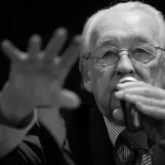 Portret starszego mężczyzny w okularach, trzymającego mikrofon. Wśród znanych reżyserów polskich, jego postać budzi szacunek.