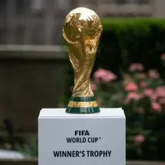 Złote trofeum FIFA World Cup na białym postumencie, z zielonym pasem i napisem "FIFA WORLD CUP".