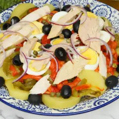 Deliciosa ensalada de patata con atún, huevo duro, pimientos asados, aceitunas negras y cebolla morada.