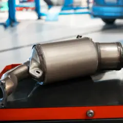 Nowy dpf w samochodzie czeka na montaż. Metalowy element układu wydechowego leży na wózku warsztatowym.