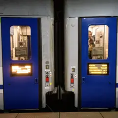 Dwa wagony kolejowe z niebieskimi drzwiami i oknami. Widać numery wagonów 16 i 15. Różne rodzaje wagonów czekają na pasażerów.