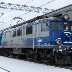 Lokomotywa EU07-421 PKP Intercity z pociągiem na tle zimowego krajobrazu. Widać elementy sieci trakcyjnej i peron.