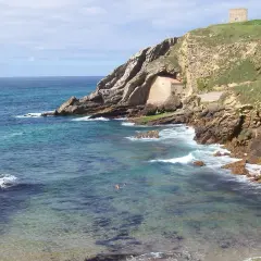 Costa rocosa y mar turquesa en Santillana del Mar, Santander. Una pequeña ermita se esconde en la roca y una torre vigía corona la colina.