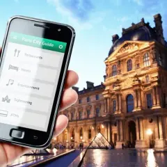 Smartfon z przewodnikiem po Paryżu w dłoni, w tle Luwr. Odkrywaj kody Francji!