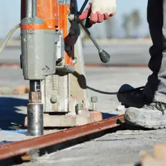 Robotnik wykonuje wiercenie dużych otworów w metalu za pomocą wiertnicy rdzeniowej.