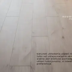 Jasne panele podłogowe ułożone równolegle do okna.