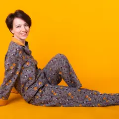 Kobieta w szarej piżamie w liski i kwiaty siedzi na żółtym tle.